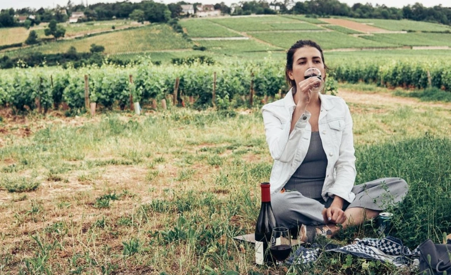 A woman who is sitting on the ground and drinking a glass of wine