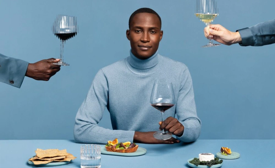 Homme habillé en bleu sur fond bleu tenant un verre de vin dans sa main