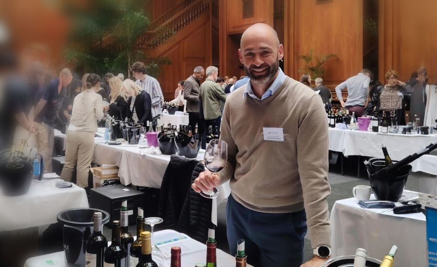 pose d'un professionnel de vin lors d'un salon et dans un espace de dégustations de vins avec d'autres professionnels derrière lui